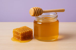 Pote de mel com favo e colher de madeira sobre mesa clara, representando os benefícios do mel.